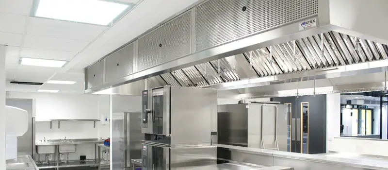 Stainless-steel canopy exhaust hoods with baffle filters over combination ovens in a bright commercial kitchen