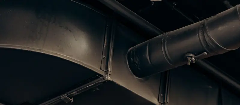 Large round and rectangular metal exhaust ducts running along a dark ceiling