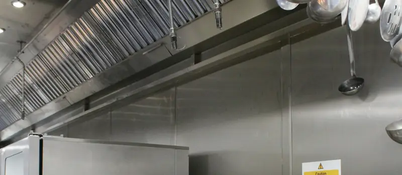 Baffle grease filters along a stainless-steel exhaust hood above deep fryers in a commercial kitchen